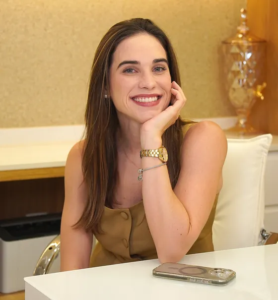 Luiza Vercezi sorrindo, apoiada na mesa do consultório